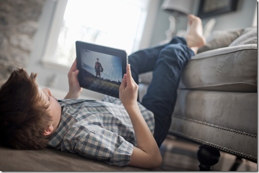 A boy lying on his front on the floor, looking at a digital tablet.