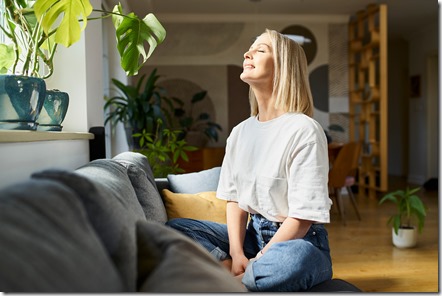 Woman enjoying the brightness and the warm of the sunshine poring into the windows of her home