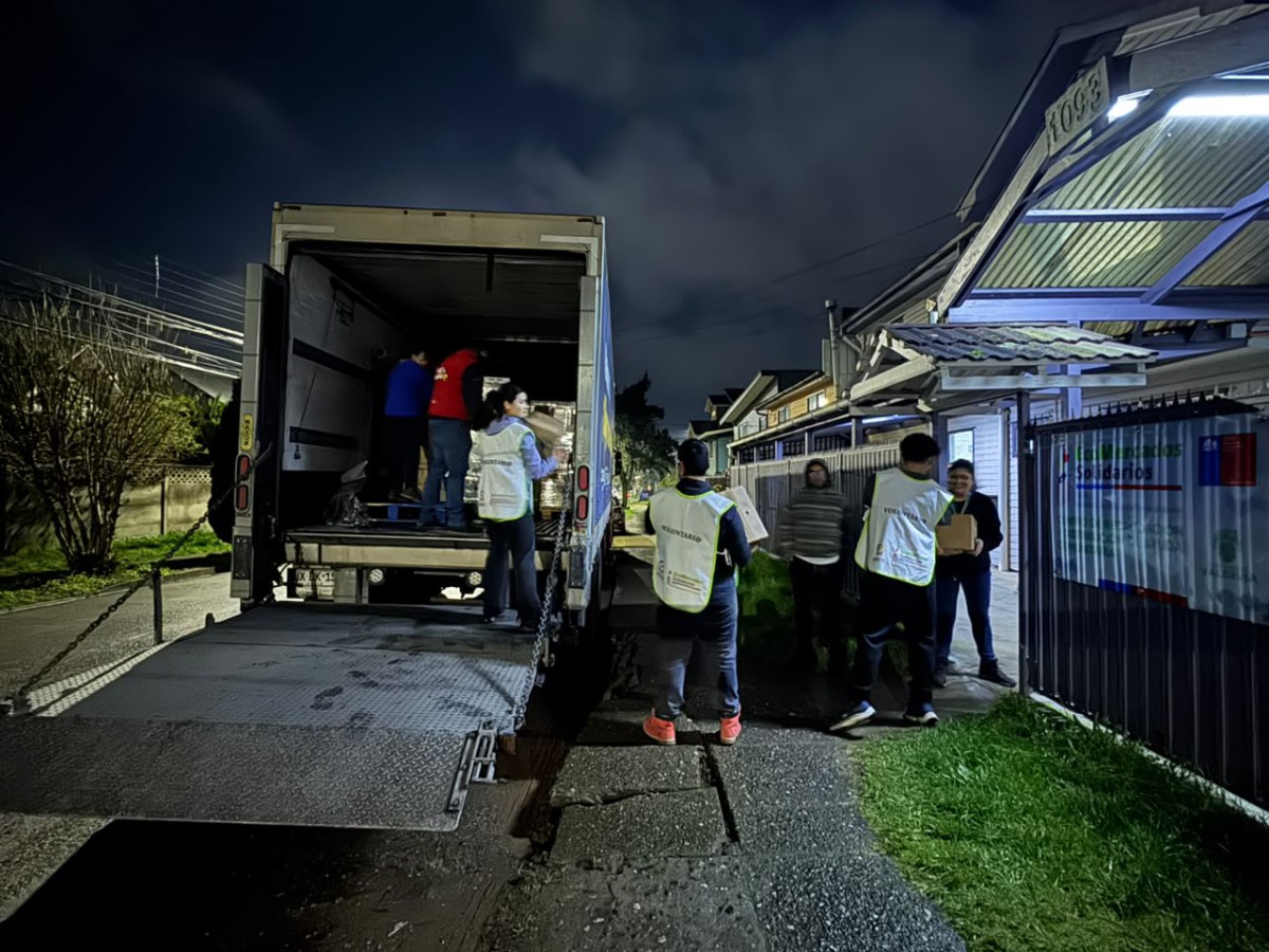 Voluntarios y personal municipal descargando cajas de ayuda humanitaria de un camión de Walmart Chile para familias afectadas por temporales en Valdivia.
